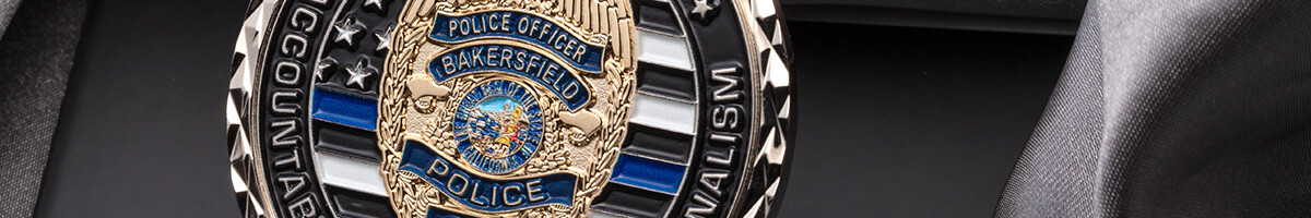 Close crop of a black and silver police coin with a high polish gold Bakersfield Police Officer badge raised at its center