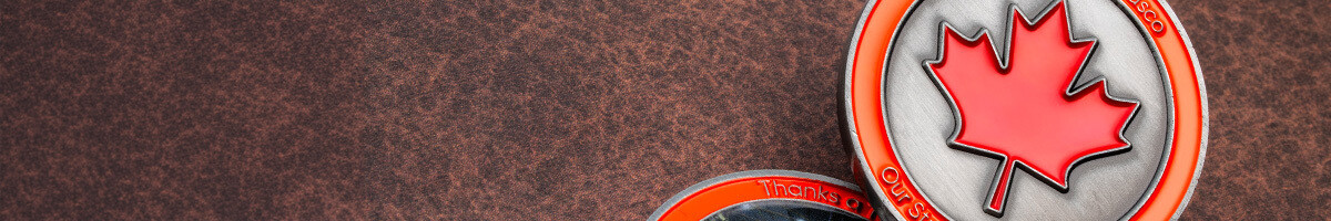 Close-up of the ArcelorMittal Dofasco coin's red enamel maple leaf on a brushed pewter field with an orange rim