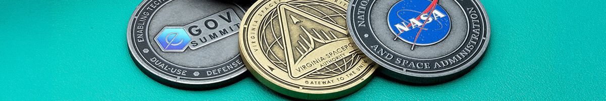 Three overlapping coins: a GovSummit dual-use defense coin, a gold Virginia Spaceport Authority Gateway to the Universe coin, and a NASA coin with the blue meatball logo