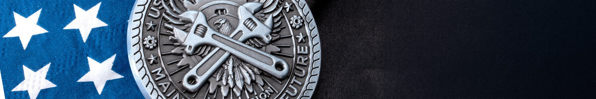 Close crop of an antique silver USPS round coin showing crossed adjustable wrenches over an eagle and the words Maintaining the Future