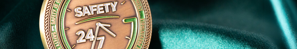 Close-up of an antique copper Safety 24/7 challenge coin with a clock face and green enamel accents