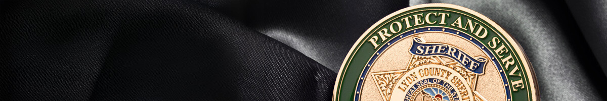 Close-up of a Lyon County Sheriff Protect and Serve challenge coin in gold with green enamel on black satin
