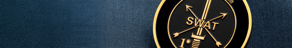 Close-up of a black and gold NEMLEC SWAT coin showing the sword and crossed arrows insignia